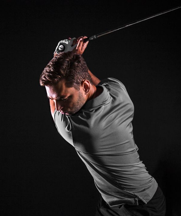Man in gray shirt swinging a golf club against a black background.