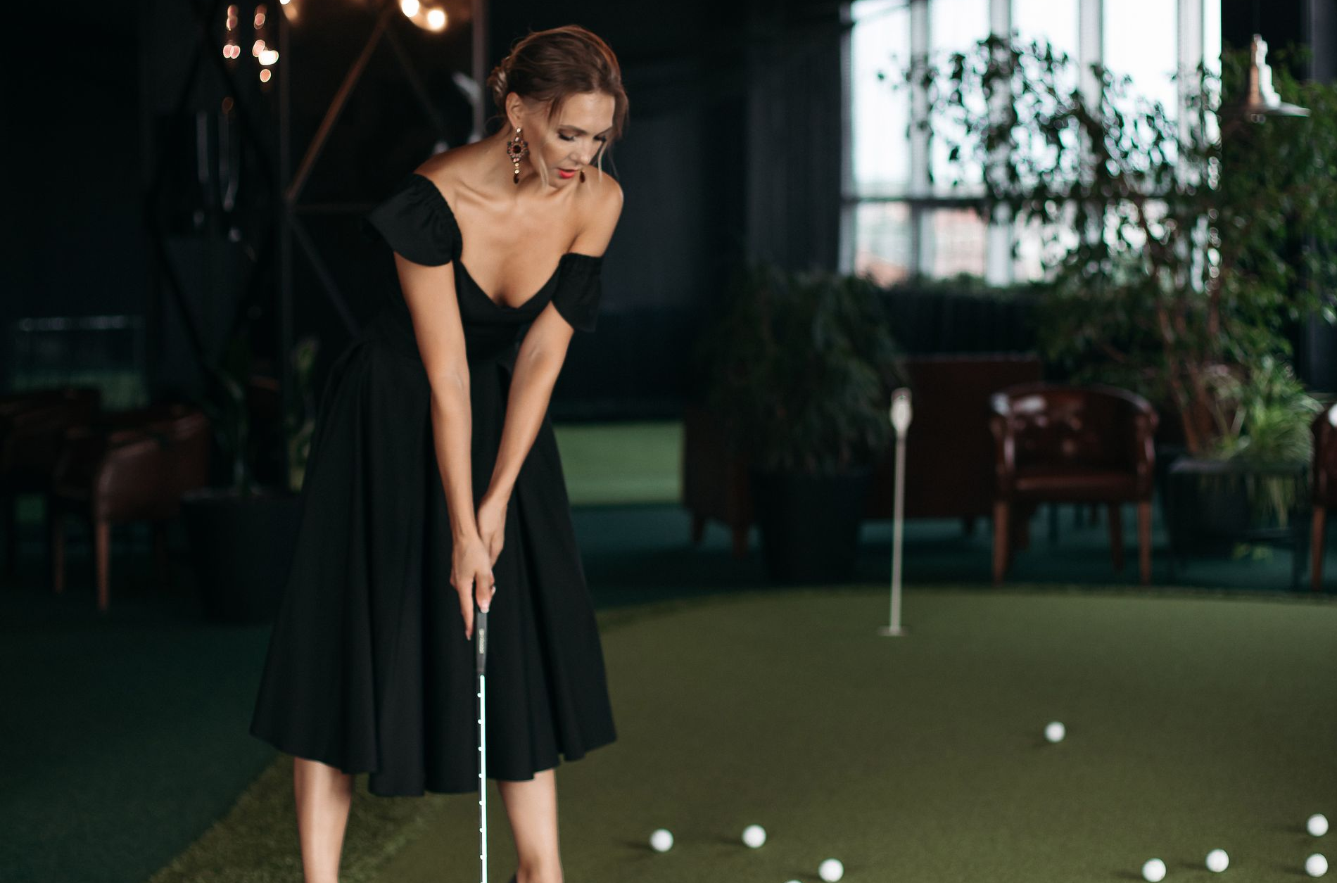 Woman in black dress putting golf ball indoors.