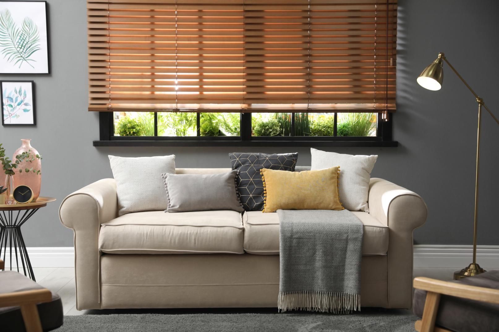 Cozy living room with beige sofa, pillows, window blinds, floor lamp, and dark rug