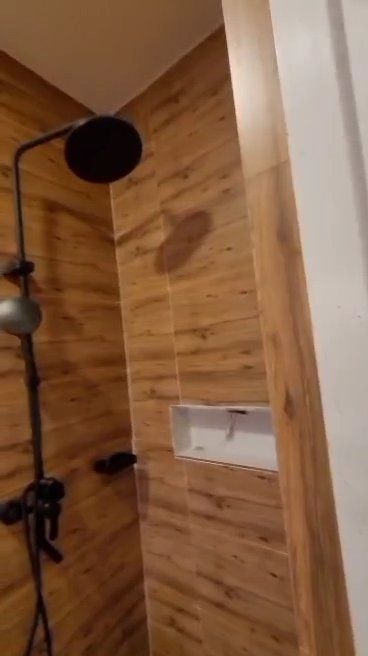 A shower with a wooden wall and a black shower head.