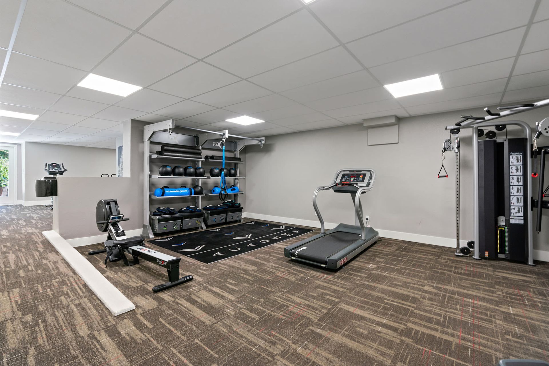 Indoor apartment community gym with a treadmill, weight rack, and workout machines.