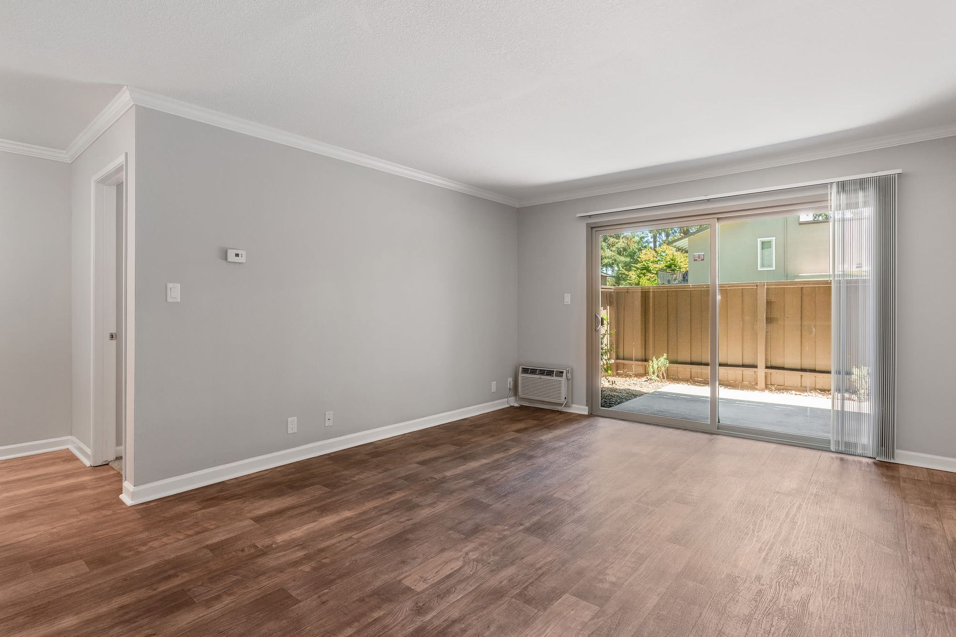 Living room with gray walls, wood-look flooring, and a sliding glass door to a fenced patio.