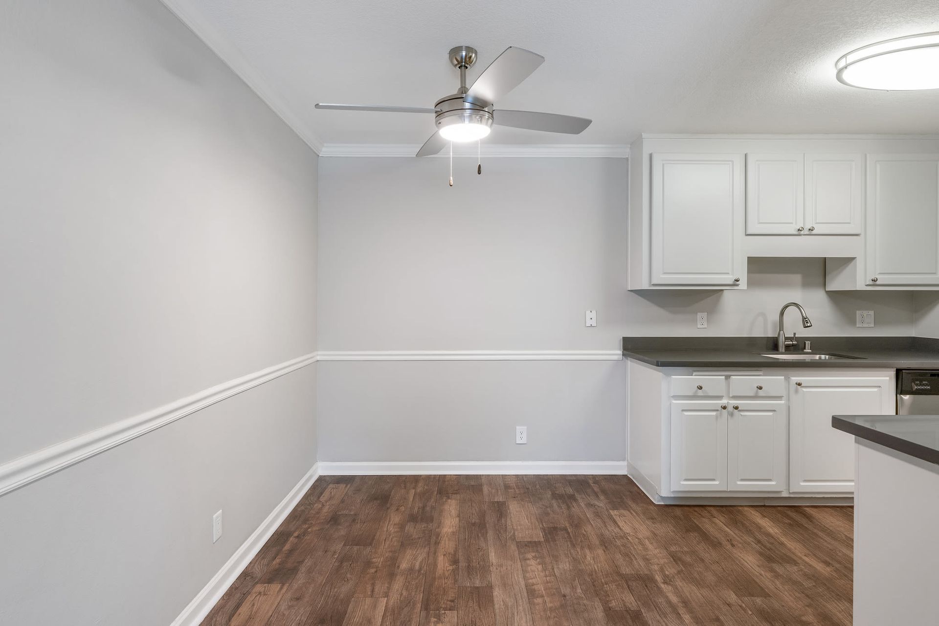 Kitchen area in an apartment with white cabinets, gray countertops, stainless sink, and wood-look flooring.