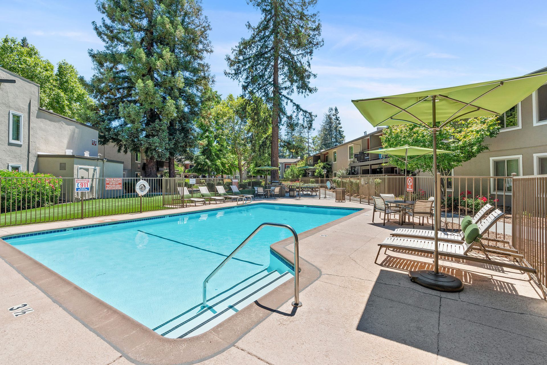 Outdoor apartment community pool with lounge chairs, tables, and green shade umbrellas.