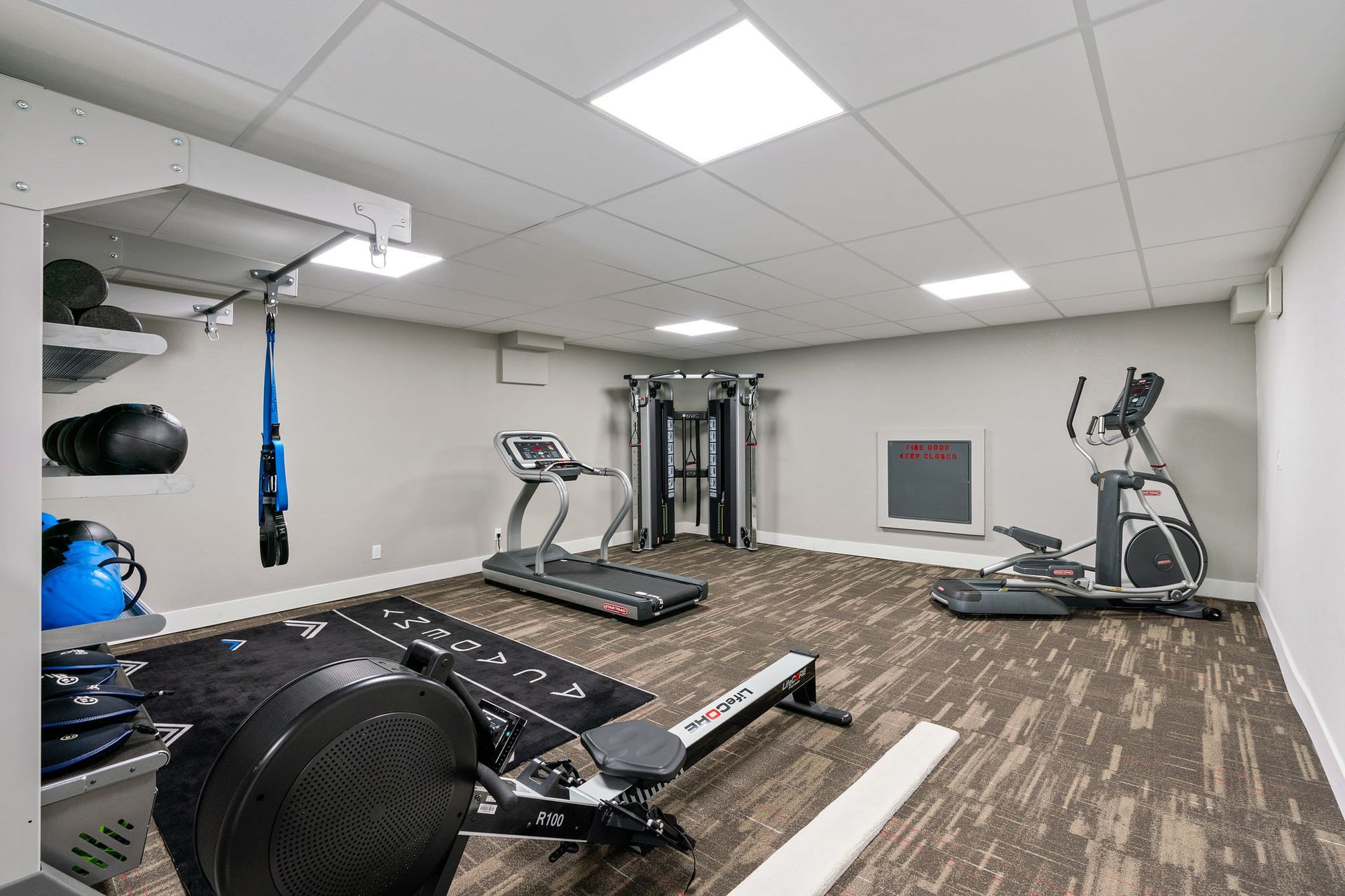 Interior of a community gym with treadmill, elliptical, weights, and a resistance station.
