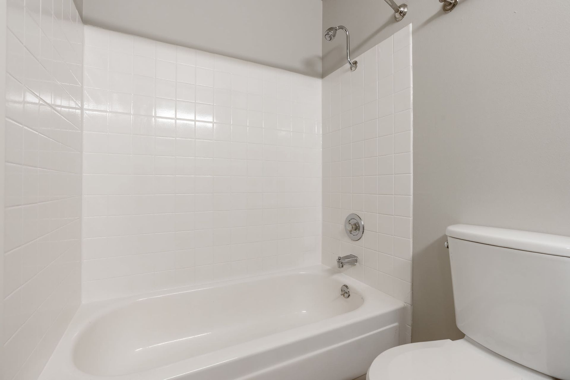 White-tiled bathroom with bathtub and chrome fixtures.