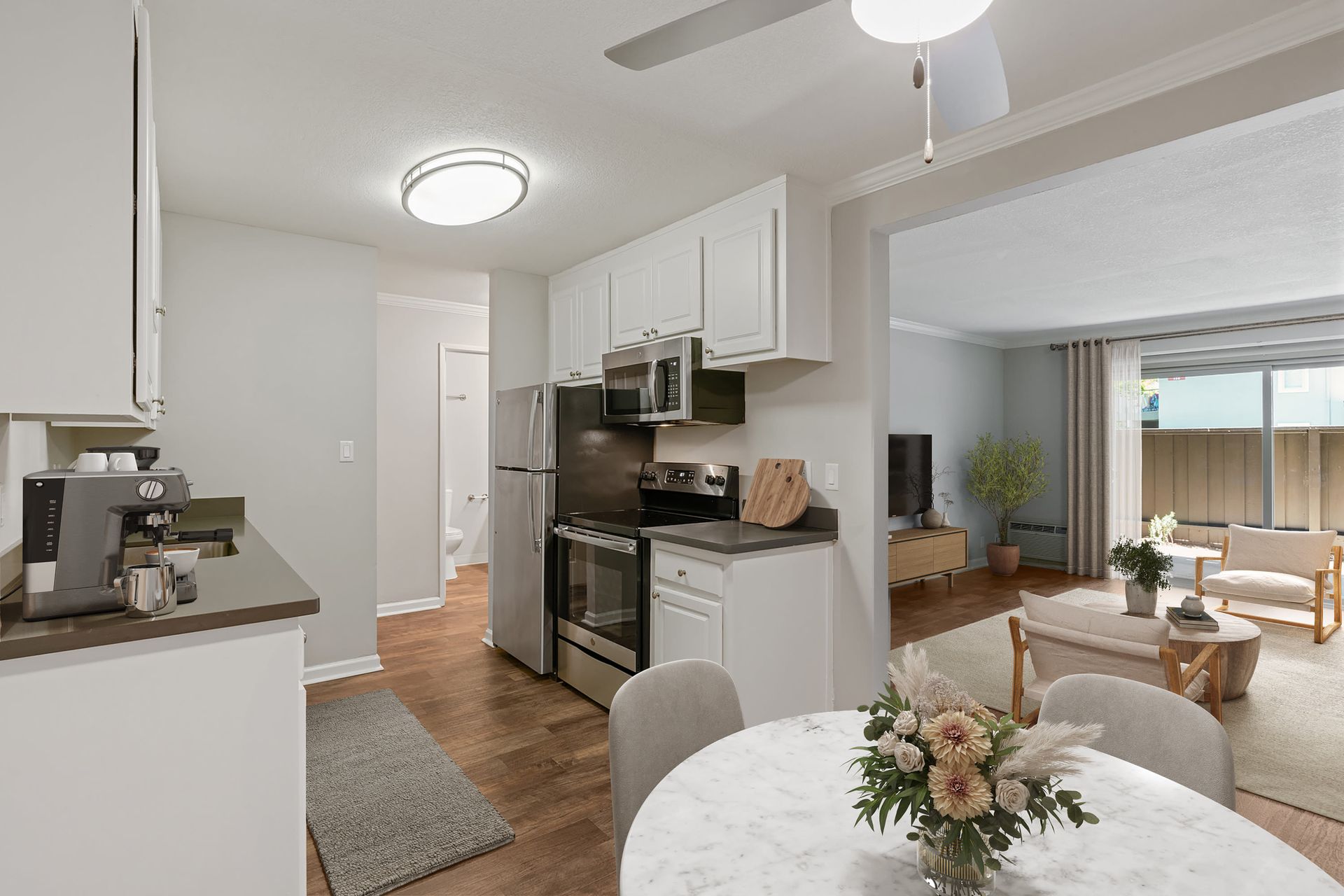 Open-concept kitchen and living area with white cabinets, stainless steel appliances, and a marble dining table.