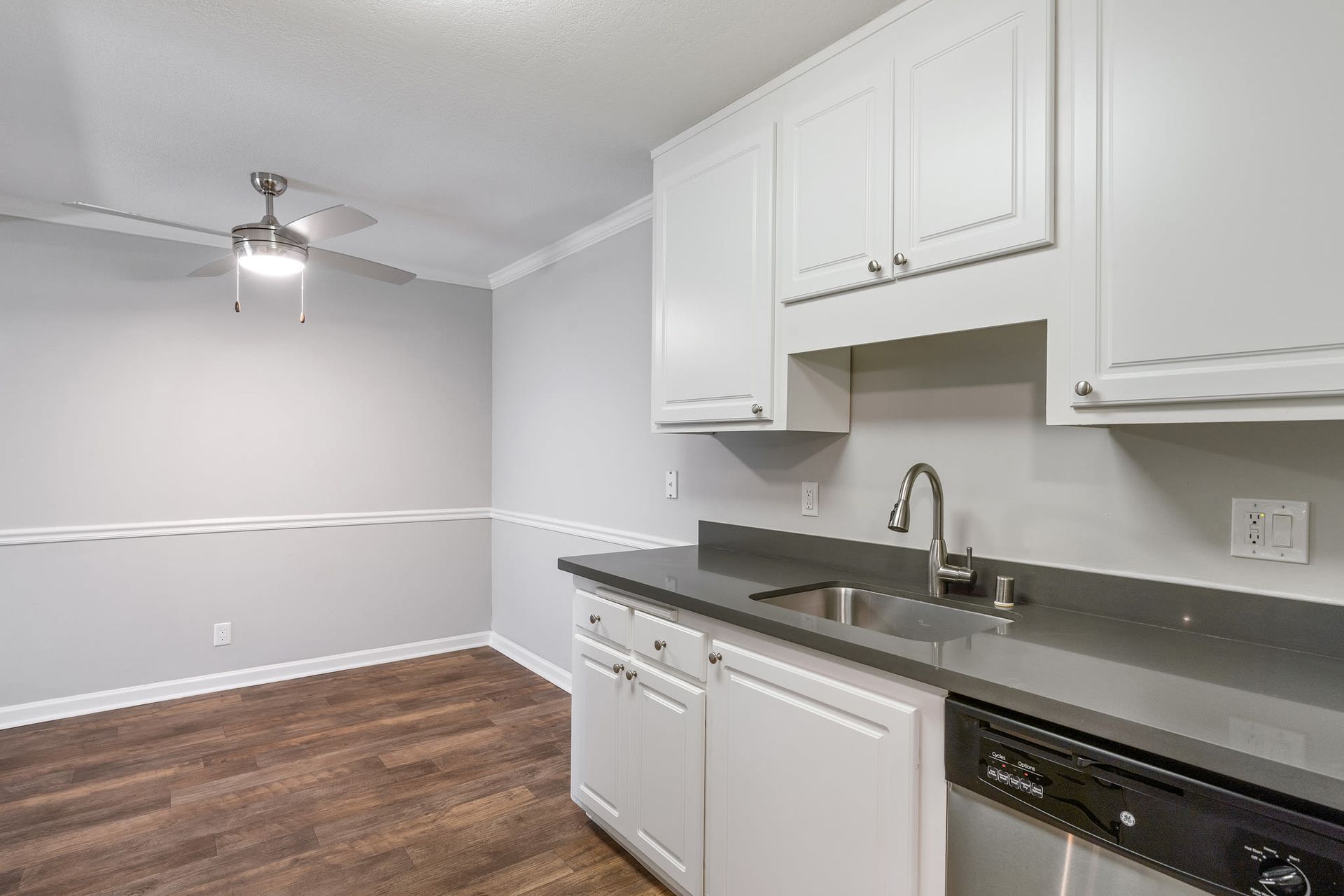 Kitchen with white upper and lower cabinets, gray countertop, stainless steel sink and dishwasher.