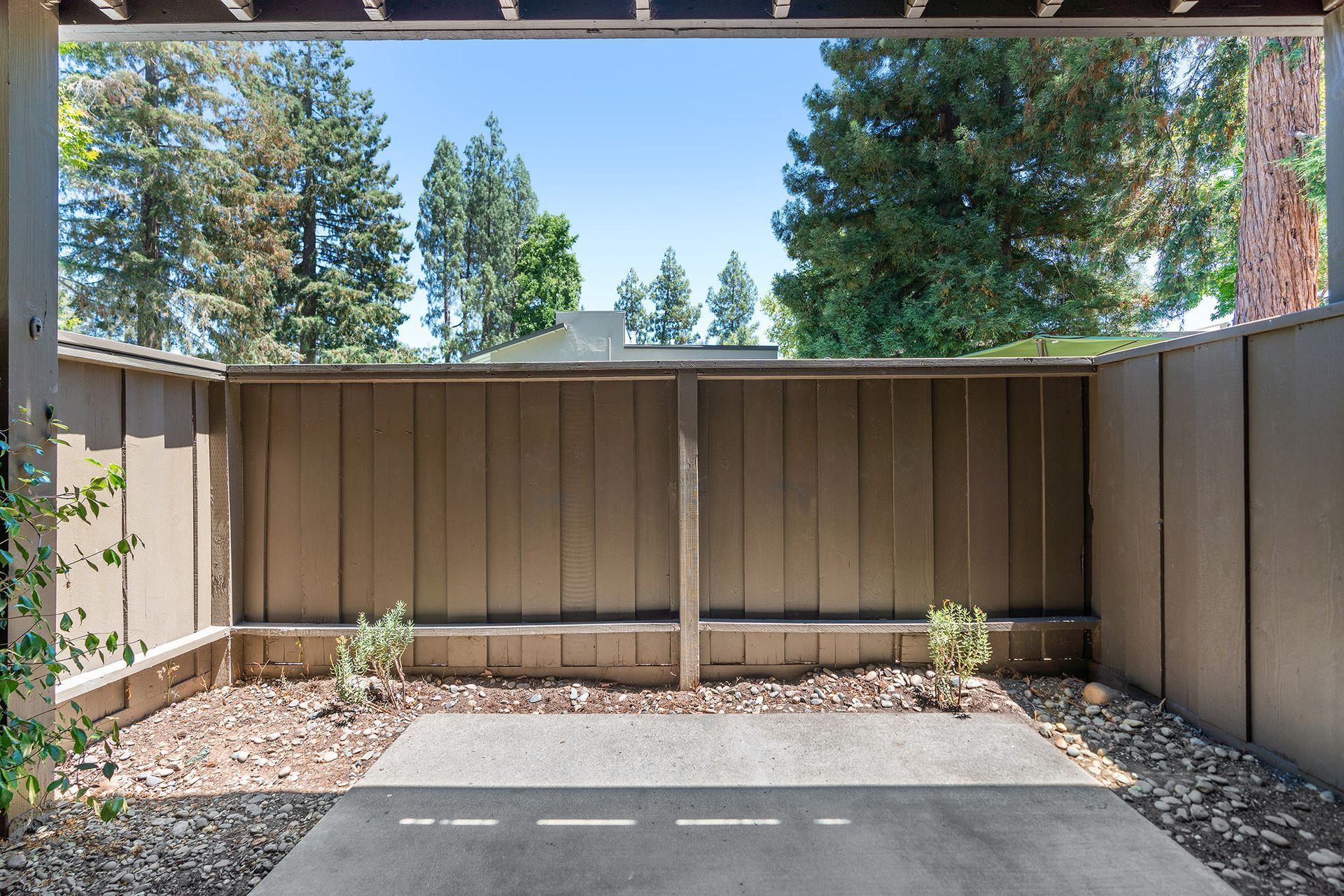 Private ground-level apartment patio with a concrete slab, brown wooden fence, and rocky edging.