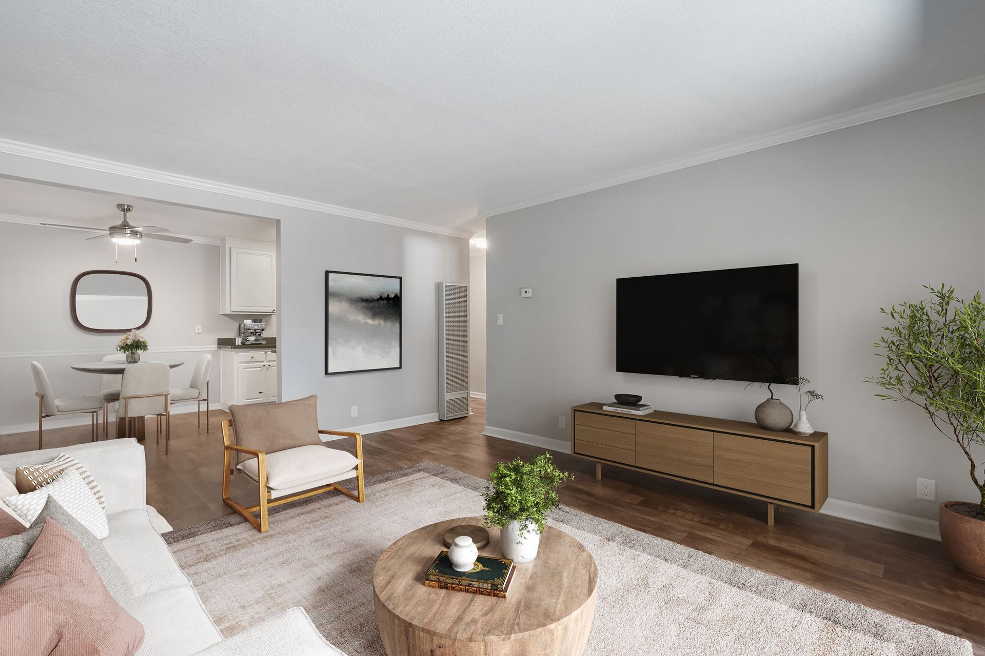 Open-plan living room with a TV on the wall, sofa, armchair, and a dining nook visible.