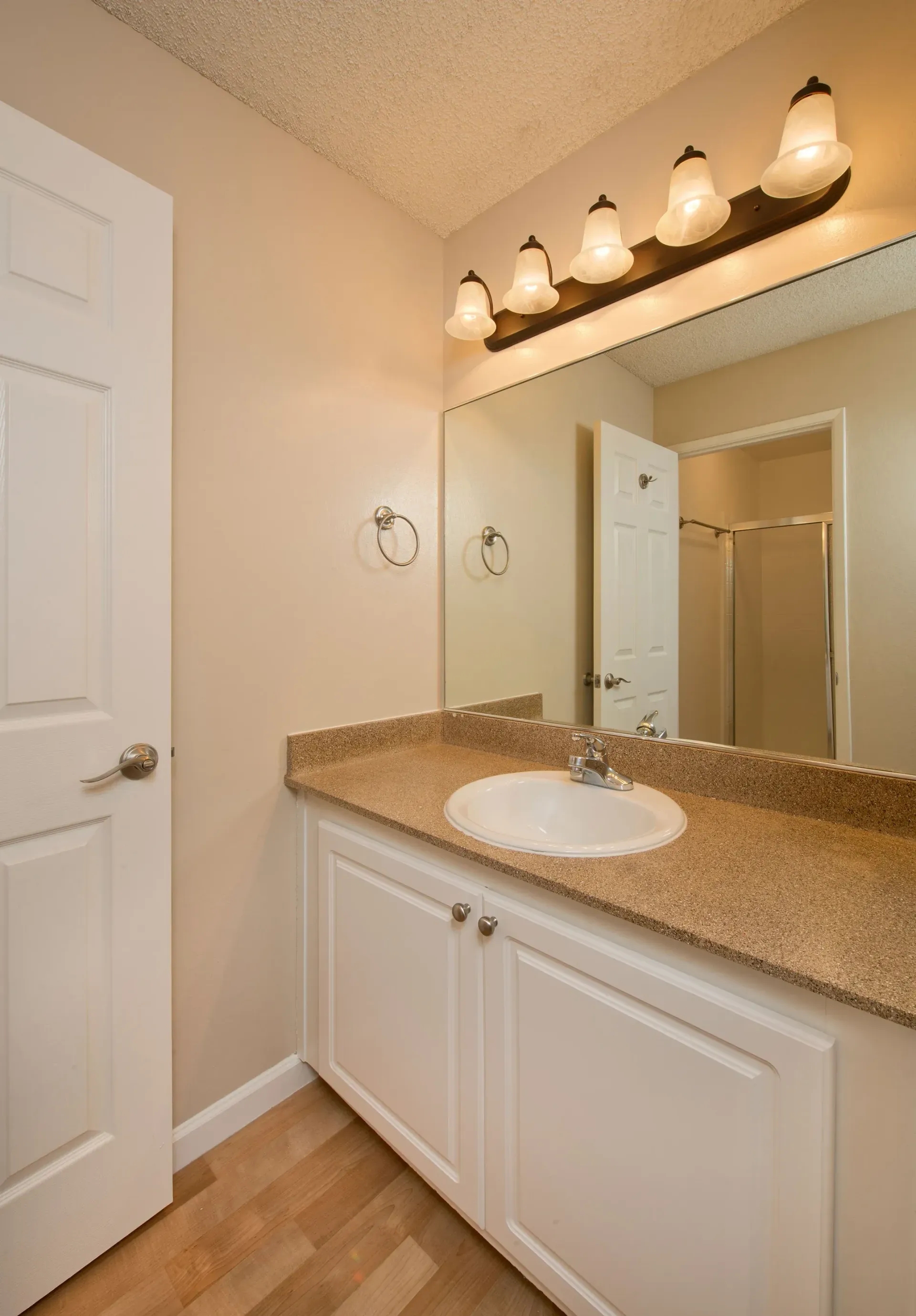 Bathroom vanity with beige countertop, white cabinetry, large mirror, and six-light fixture.
