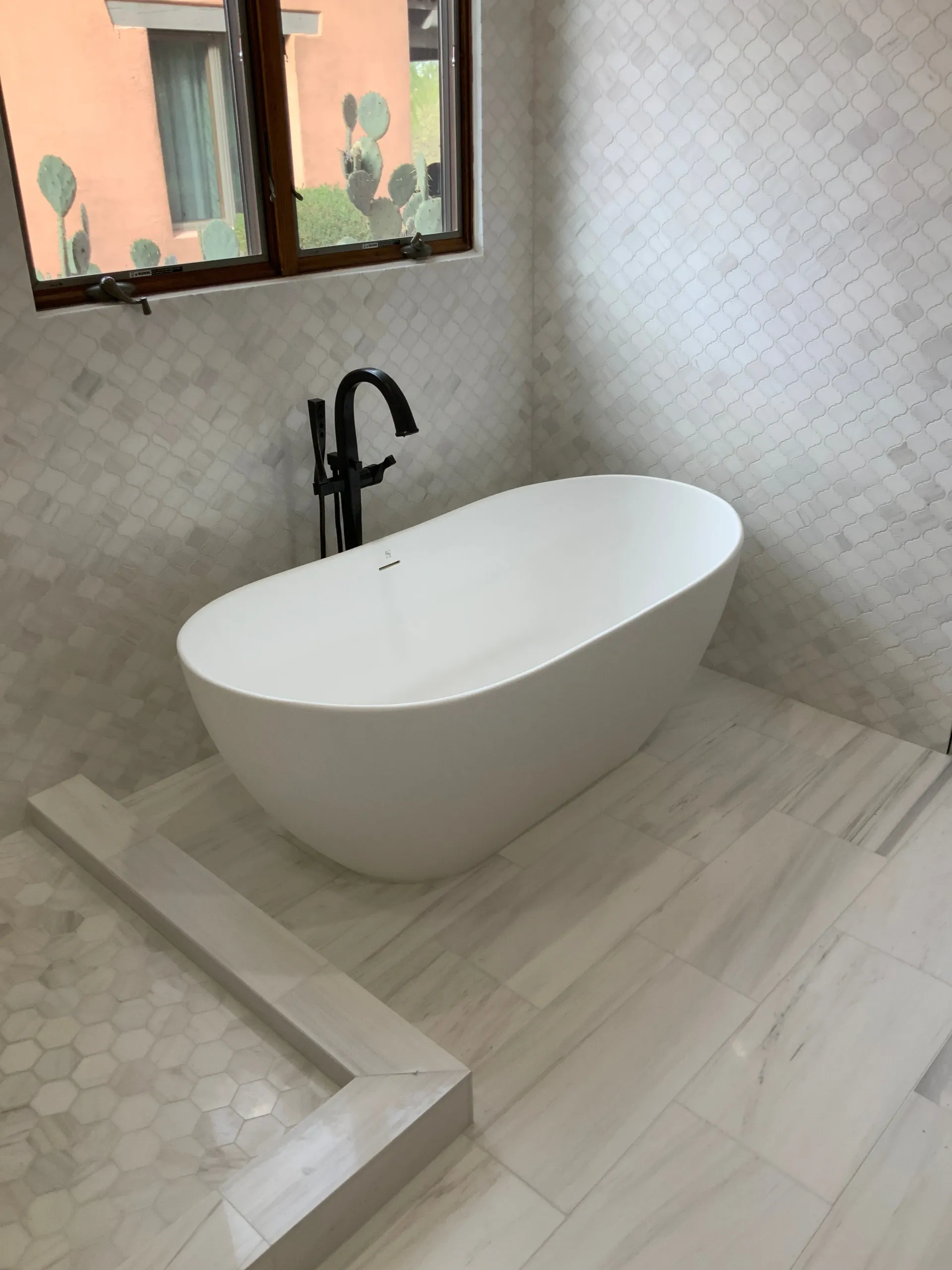Modern bathroom with a white freestanding bathtub, black faucet, and tiled walls.