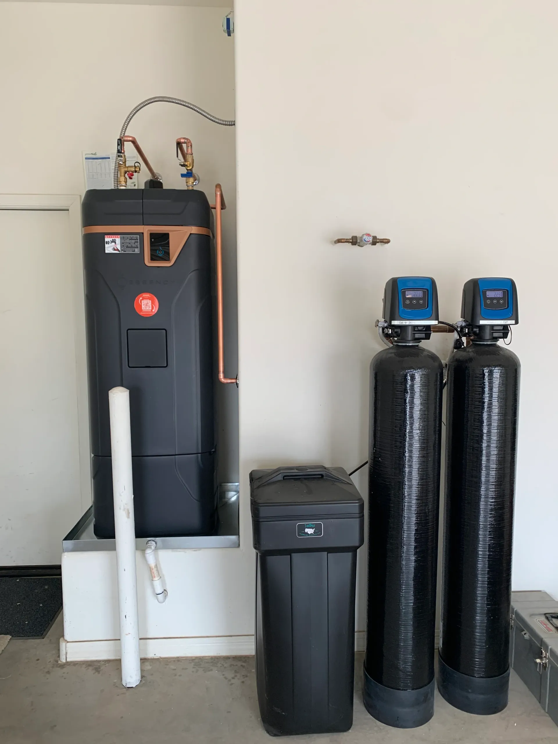 Water softener and filtration system in a utility room with black tanks and a white basin.