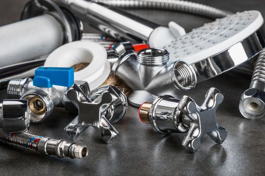 Close-up of assorted chrome plumbing fittings, valves, and shower parts on a surface. Close-up of assorted chrome plumbing fittings, valves, and shower parts on a surface.