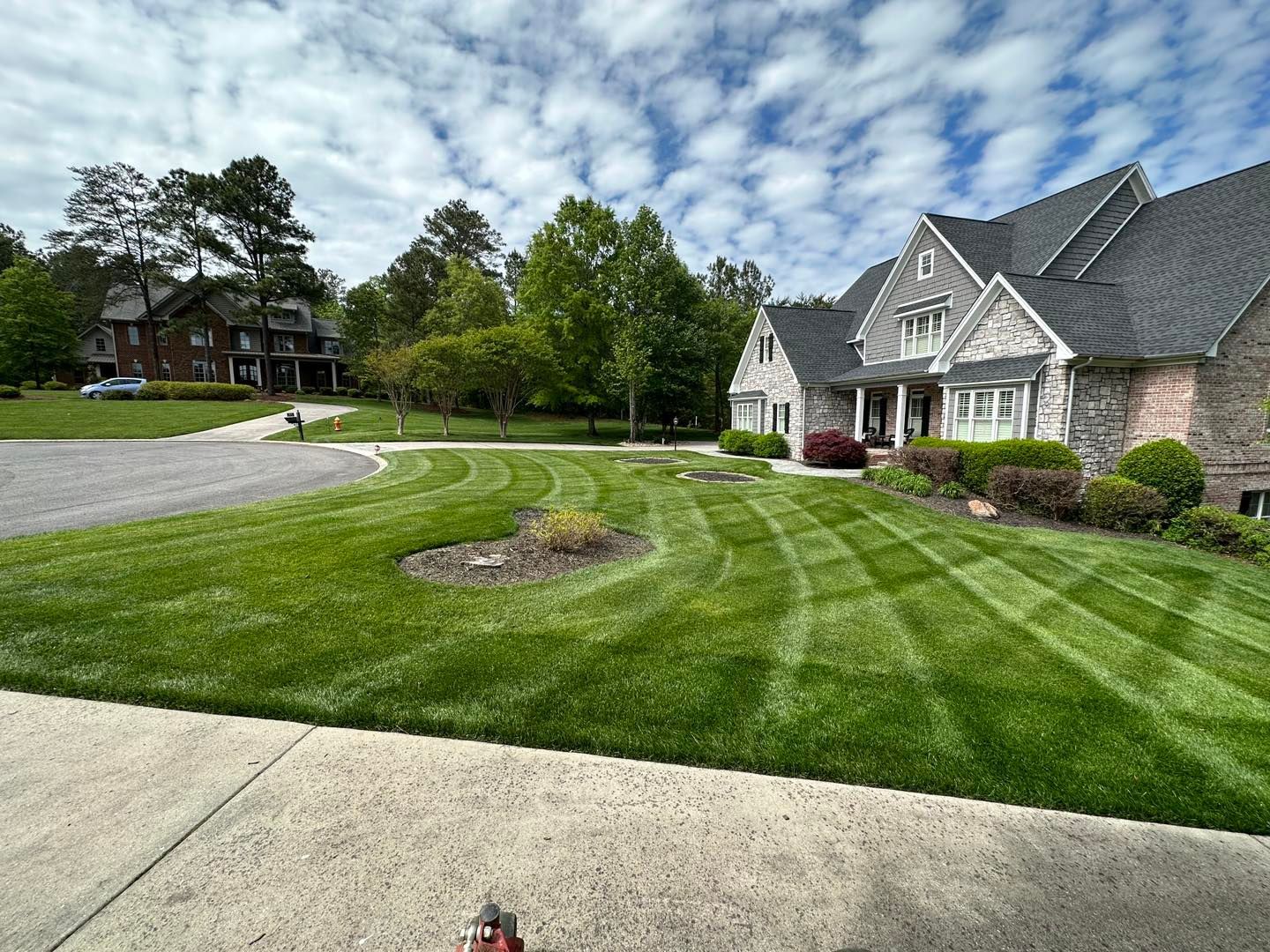 Lawn with striped mowing pattern in front of a stone house under a partly cloudy sky.