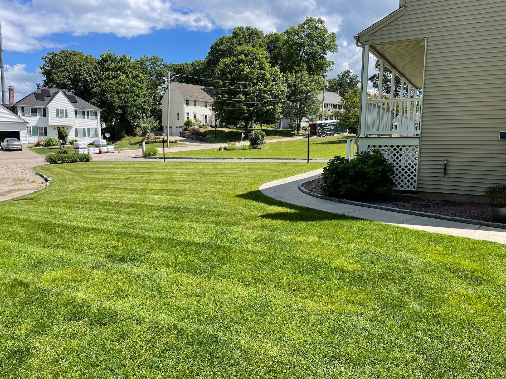 Well-manicured green lawn with houses and trees under a blue sky.