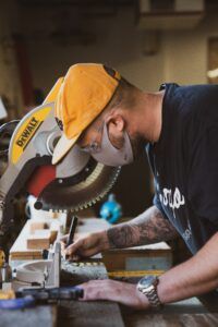A man wearing a mask is cutting a piece of wood with a circular saw.