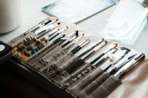 A bunch of pens are sitting on top of a newspaper on a table.