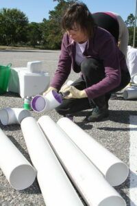A woman is kneeling down next to a pile of white pipes