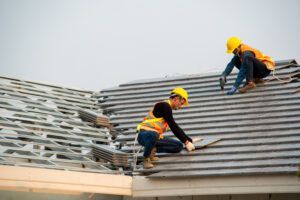 Two construction workers are working on the roof of a building.
