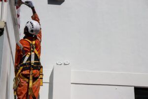 A man wearing a helmet and safety harness is working on a white wall.