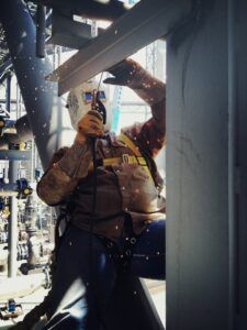 A man is welding a metal structure in a factory.