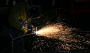 A man is cutting a piece of metal with a torch in a dark room.