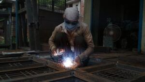 A man is welding a piece of metal in a factory.