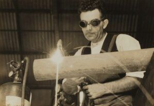 A man wearing goggles is welding a pipe in a black and white photo