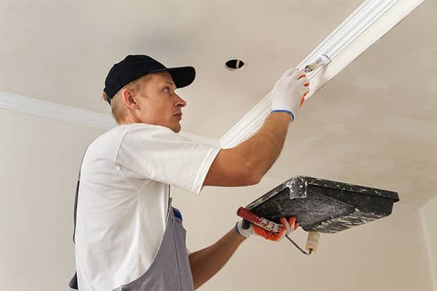 A man is painting a ceiling with a roller.
