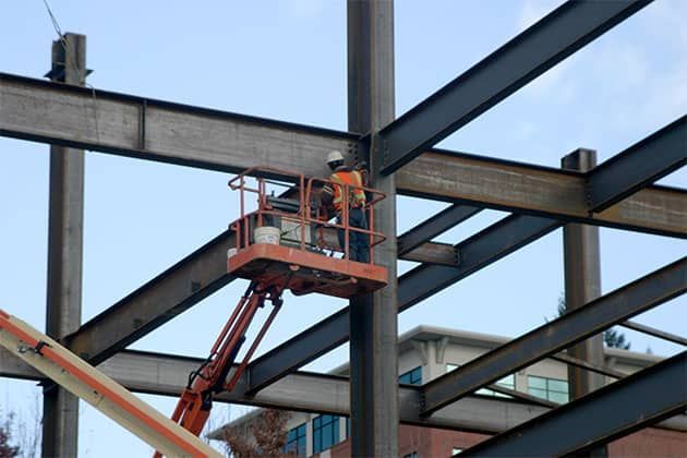 A man is standing on a lift working on a steel structure.