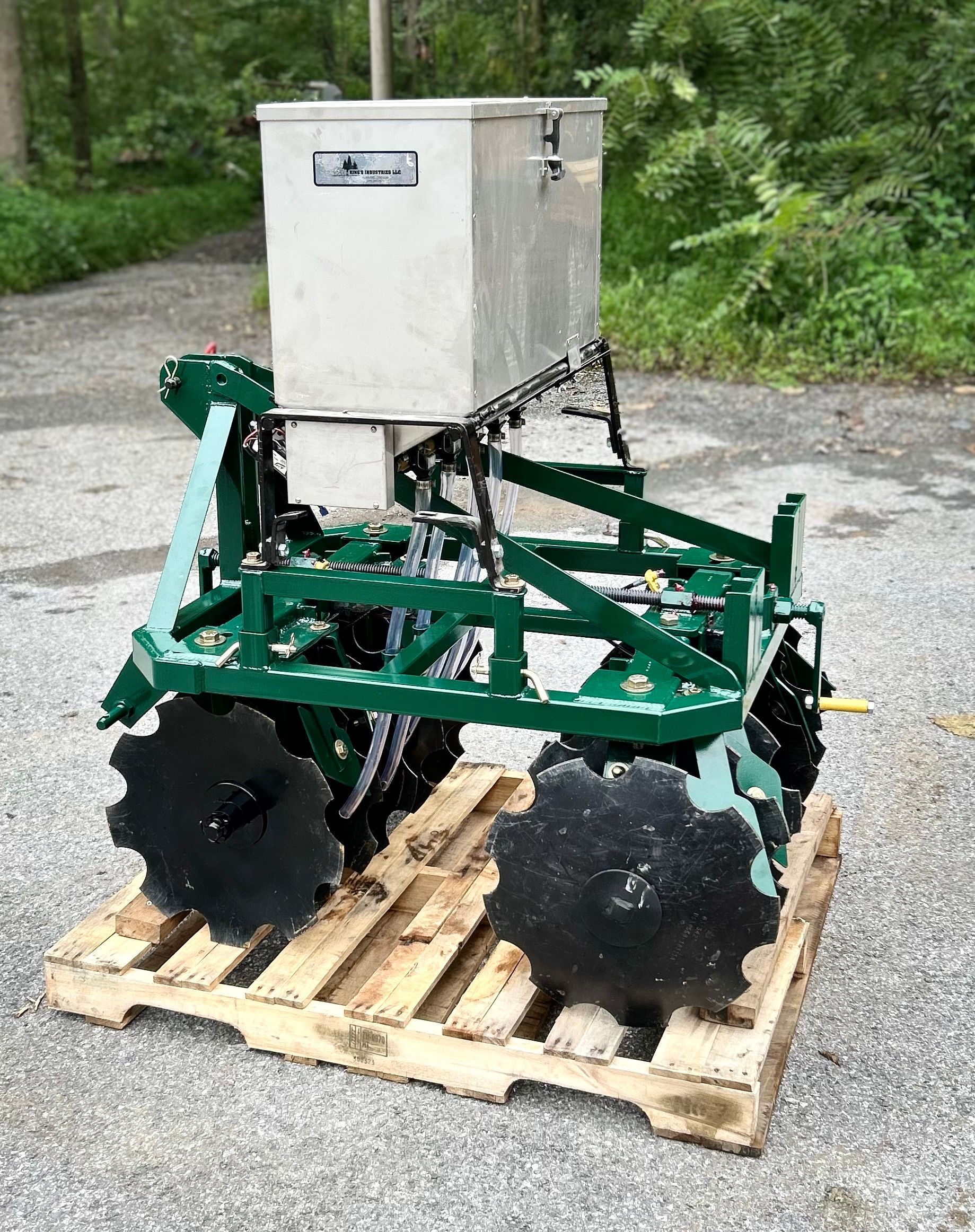 A green seeder machine with a silver container on a wooden pallet outdoors.