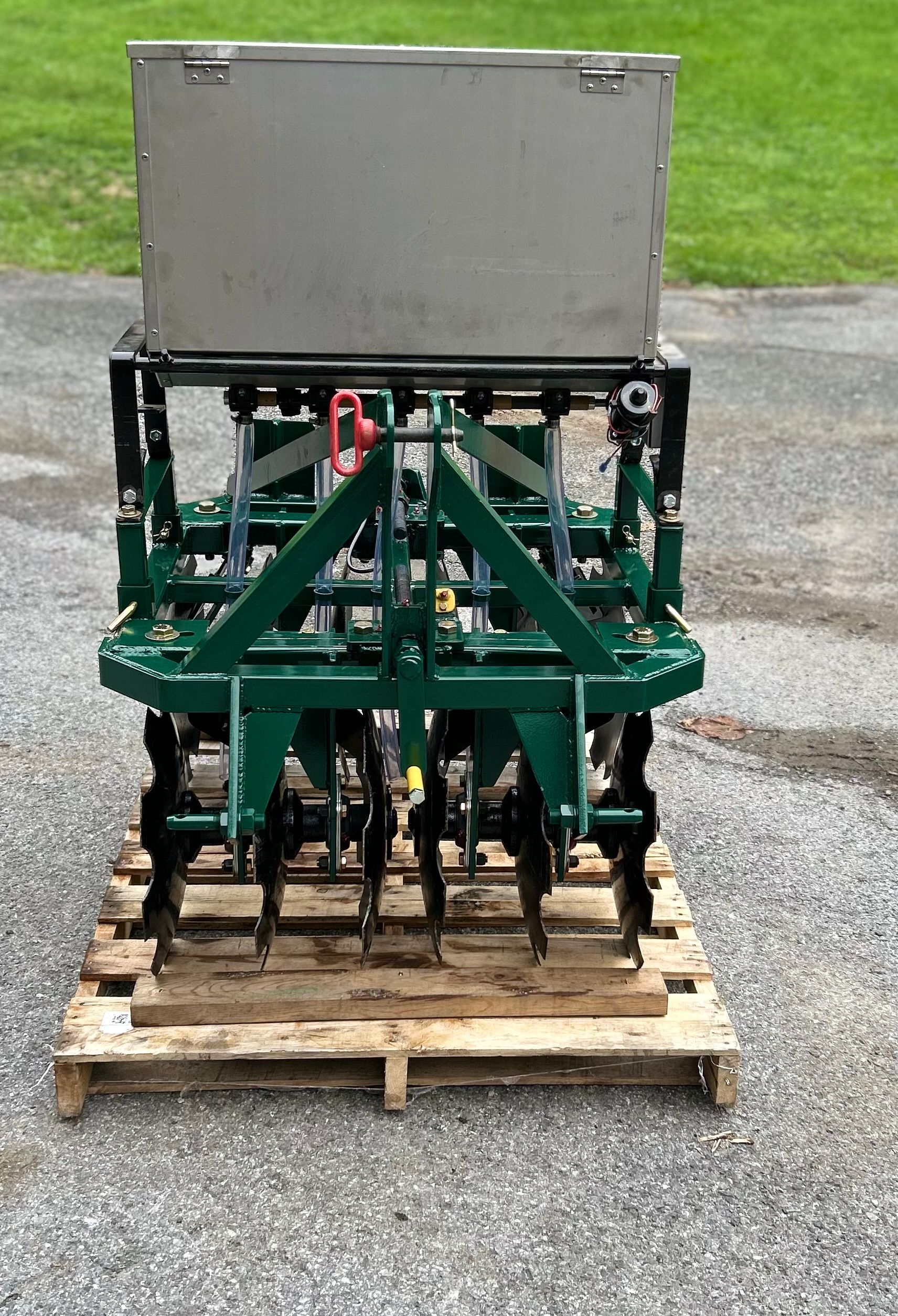 Green and silver farm implement on a wooden pallet, likely for soil preparation.