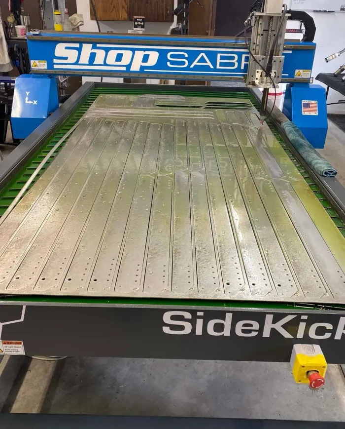CNC router cutting metal sheet with vertical lines and holes, in a workshop.