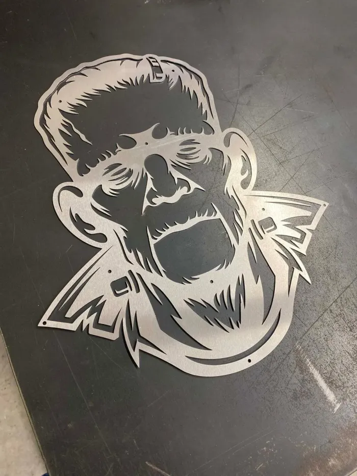 Metal cutout of Frankenstein's monster's face, open mouth, flat metal background.
