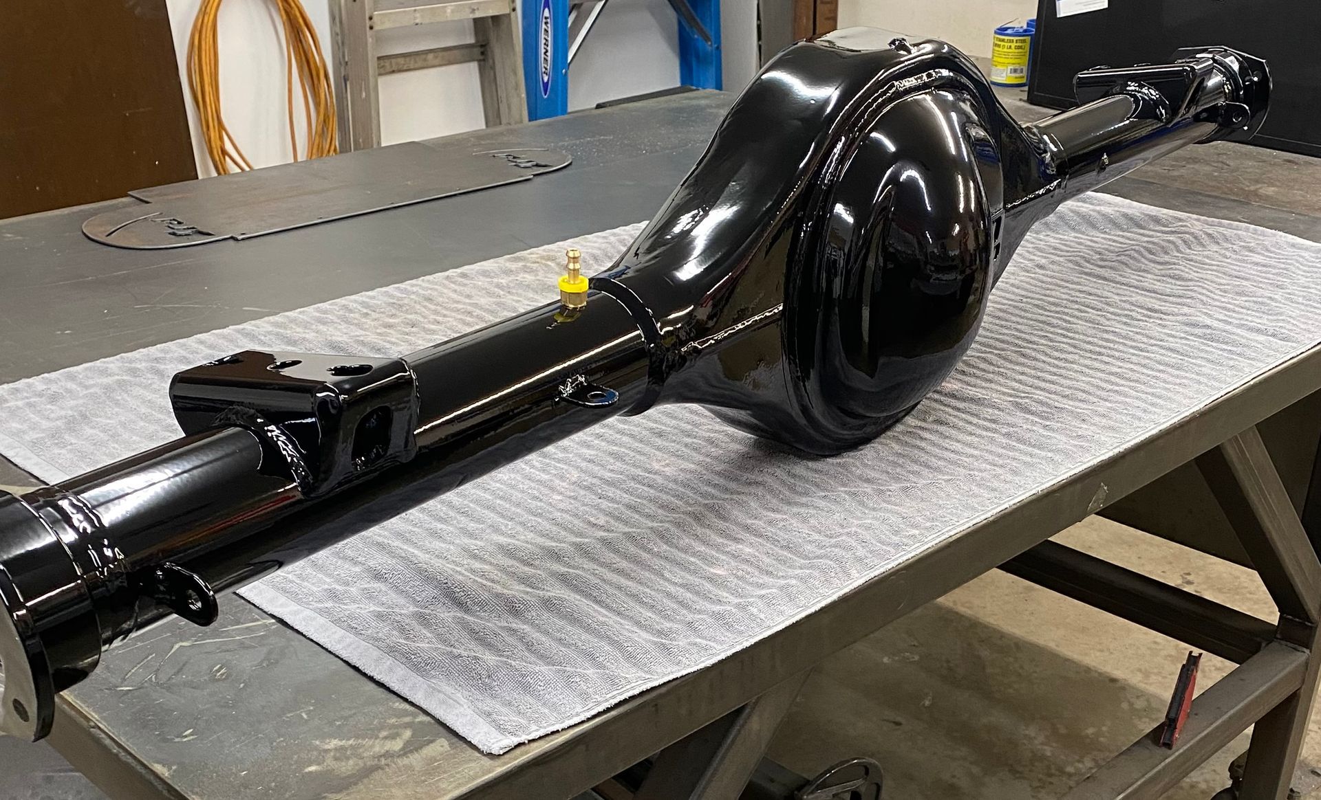 Black, freshly painted car rear axle on a workbench.