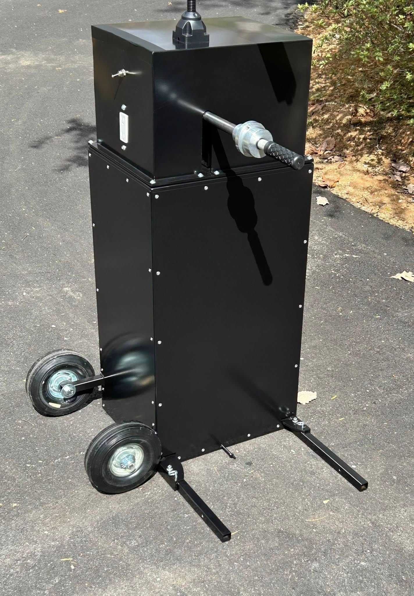 Black metal smoker with wheels and handle on pavement.