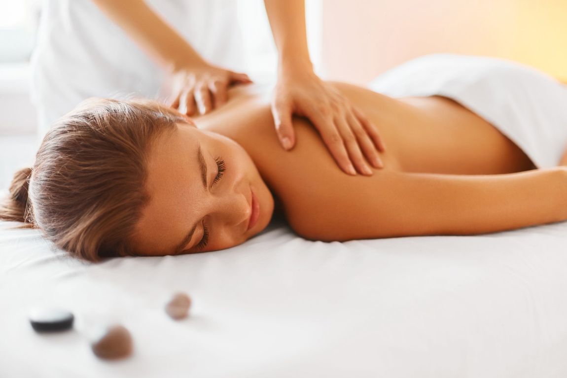 young woman laying down on relaxing massage bed wearing a towel with a massage therapist rubbing her back during a massage therapy session.