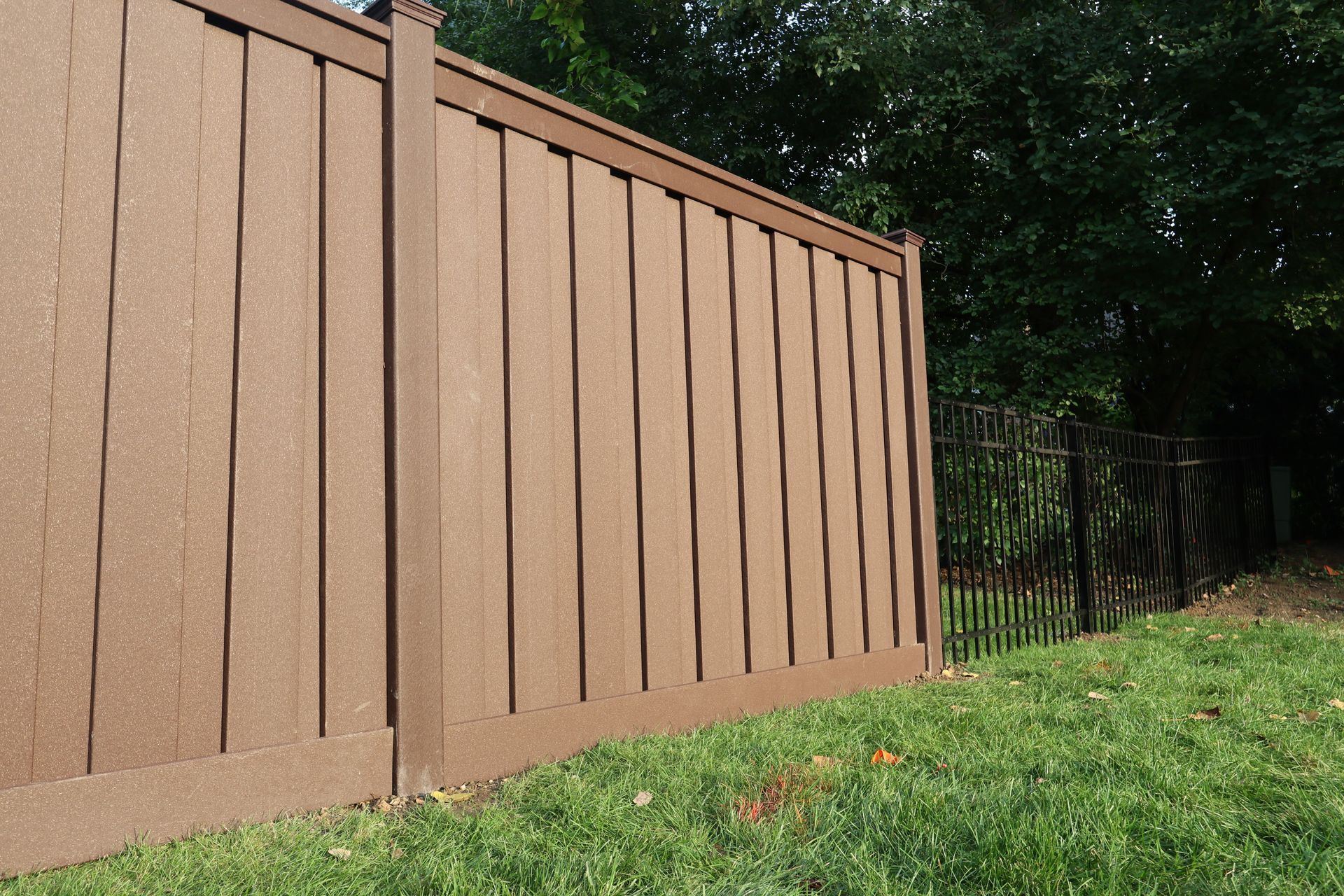 A brown composite fence surrounds a lush green yard