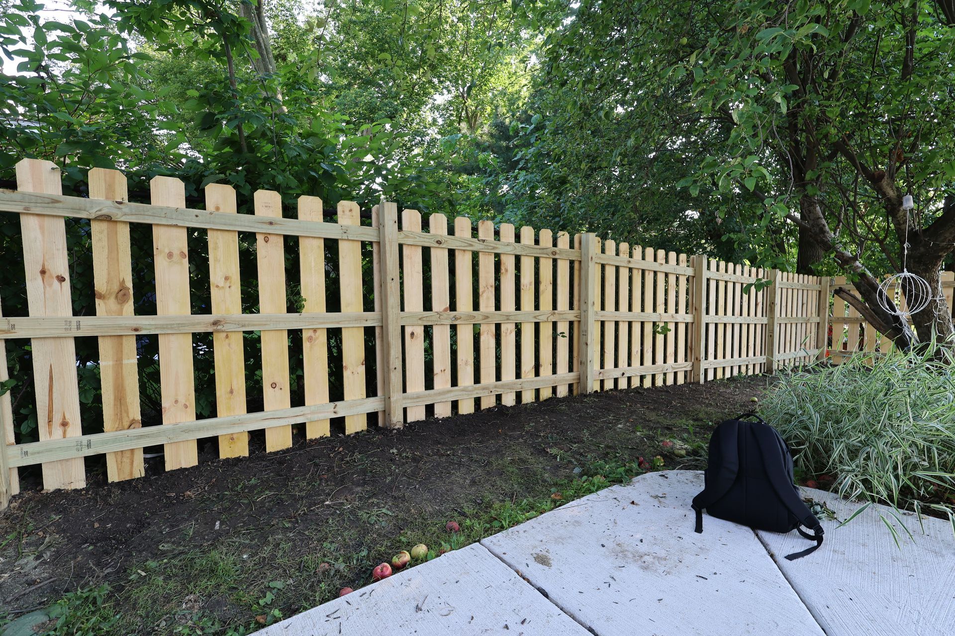 A wooden fence with a backpack sitting on the sidewalk next to it.
