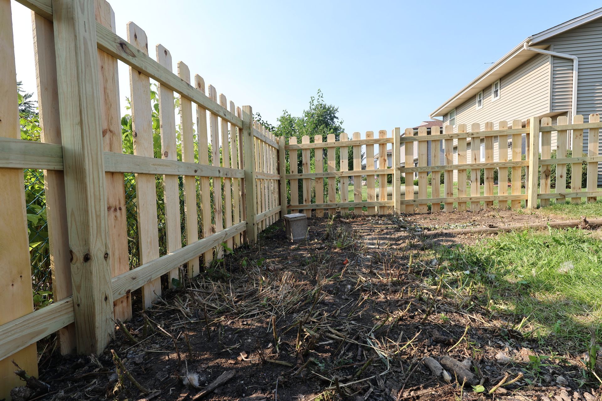 A wooden picket fence surrounds a yard with a house in the background