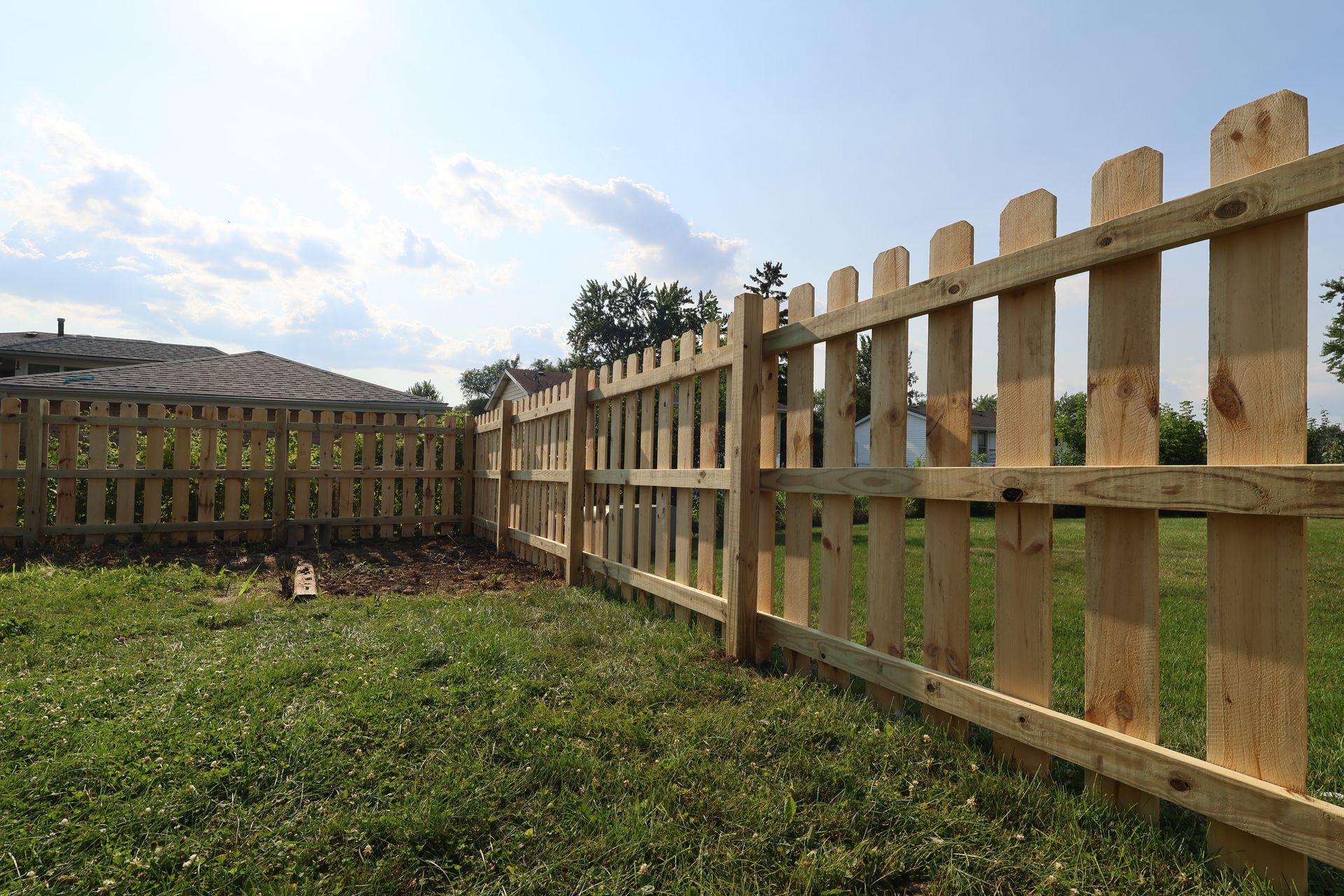 A wooden picket fence is in the middle of a grassy field.