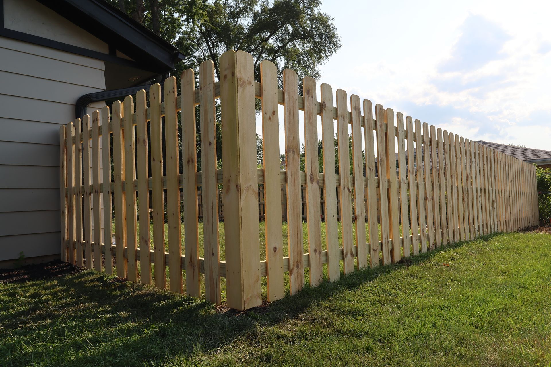 A wooden picket fence is in the backyard of a house.
