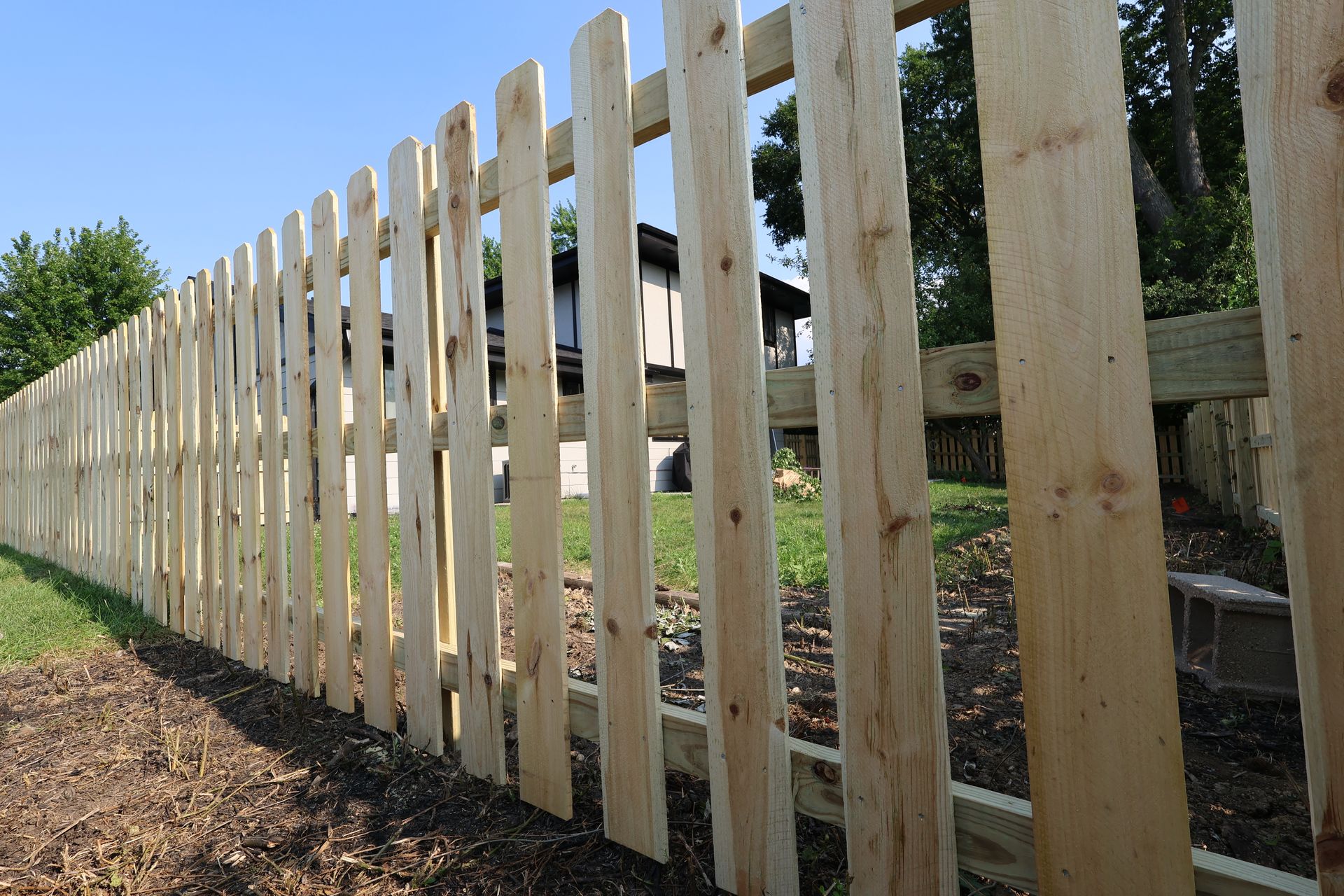 A wooden picket fence is surrounding a yard in front of a house.