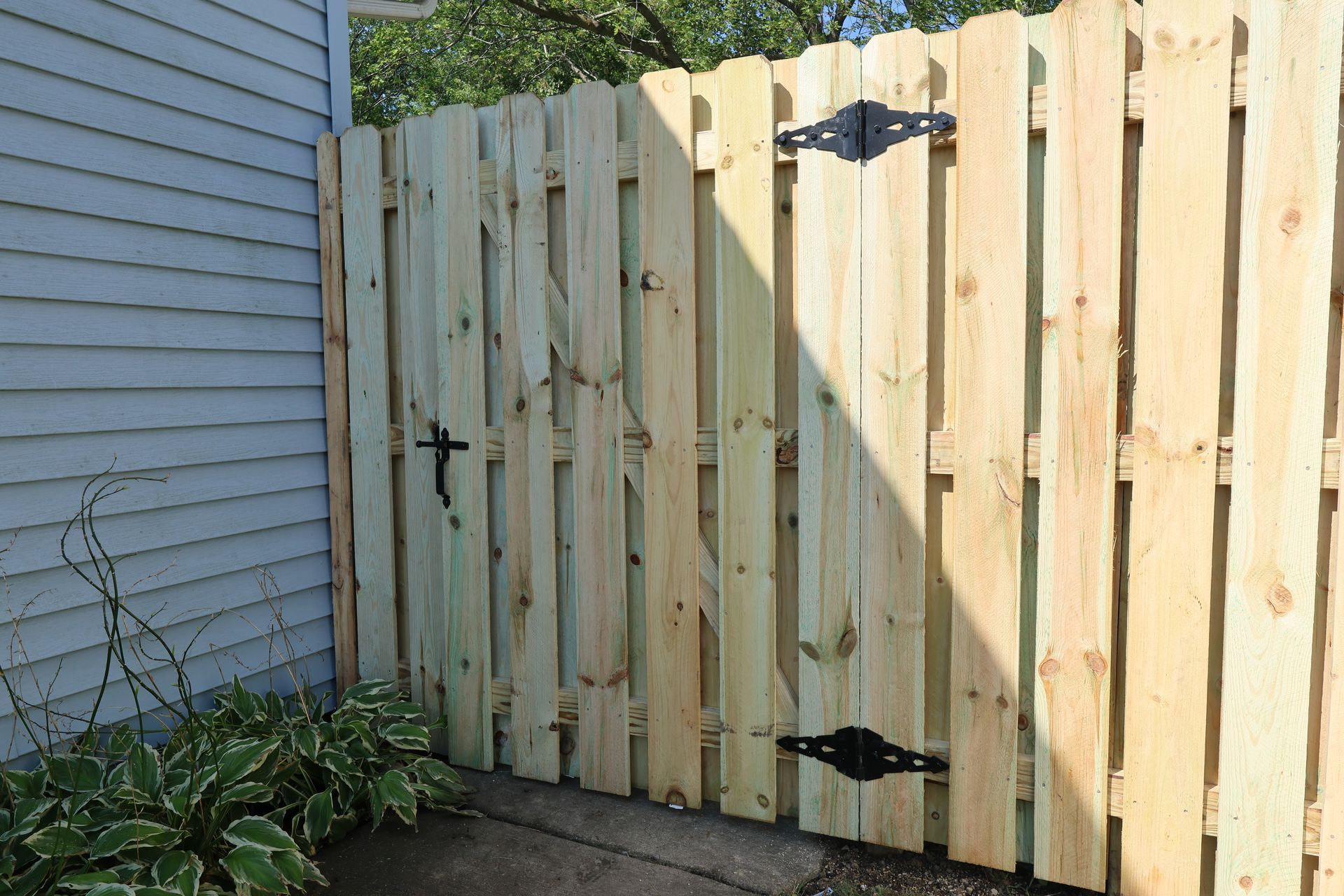 A wooden fence with a black gate is next to a house.