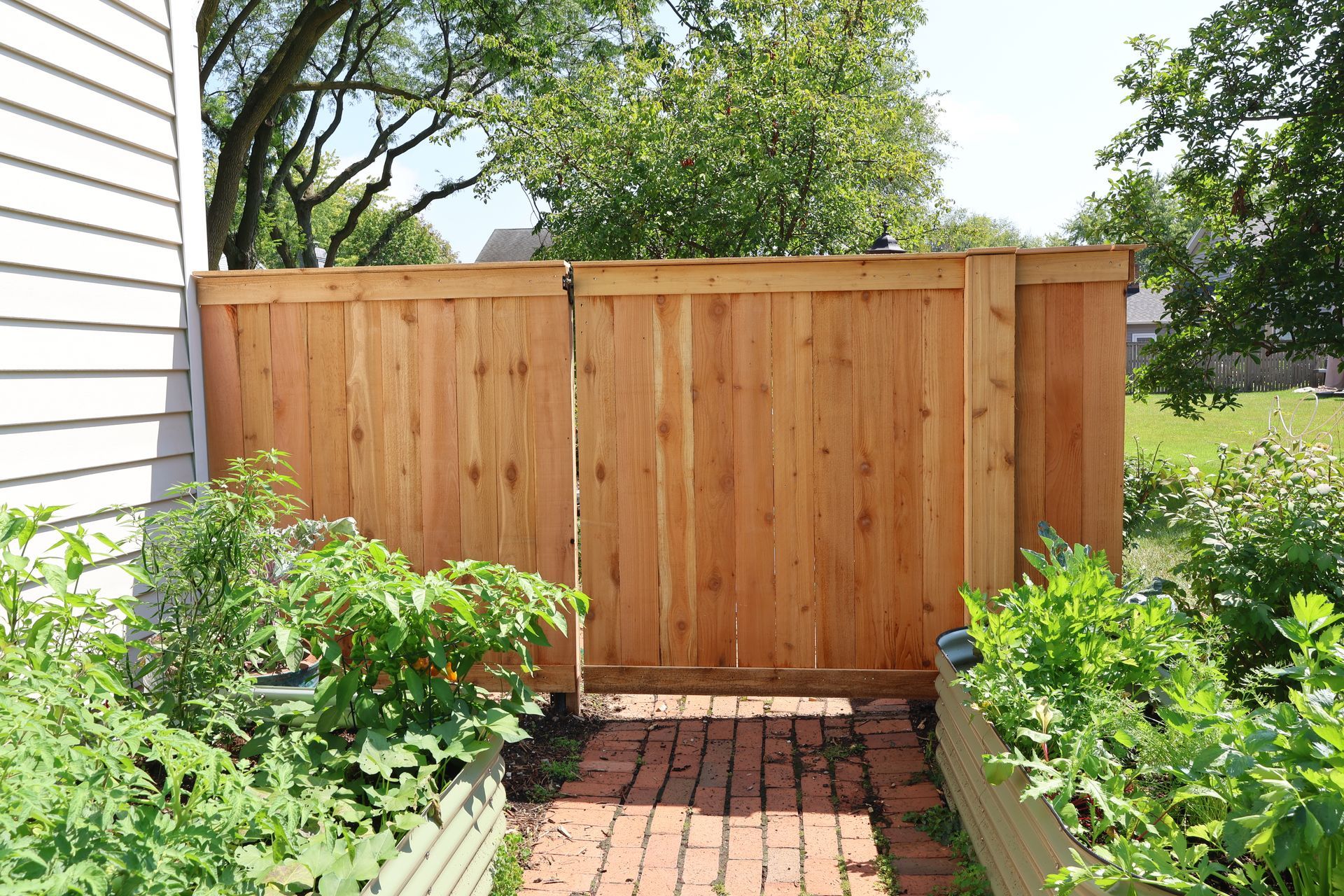 A wooden fence is surrounded by plants and a brick walkway.