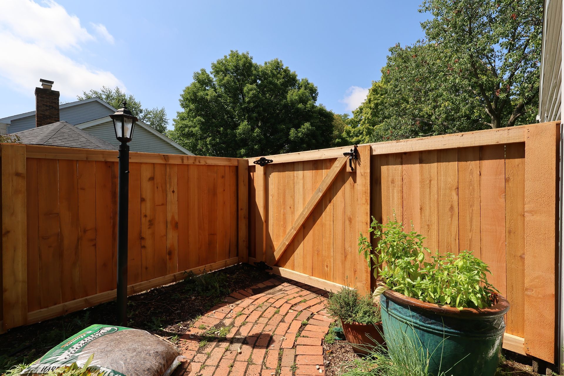 A wooden cedar fence surrounds a brick walkway in a backyard.