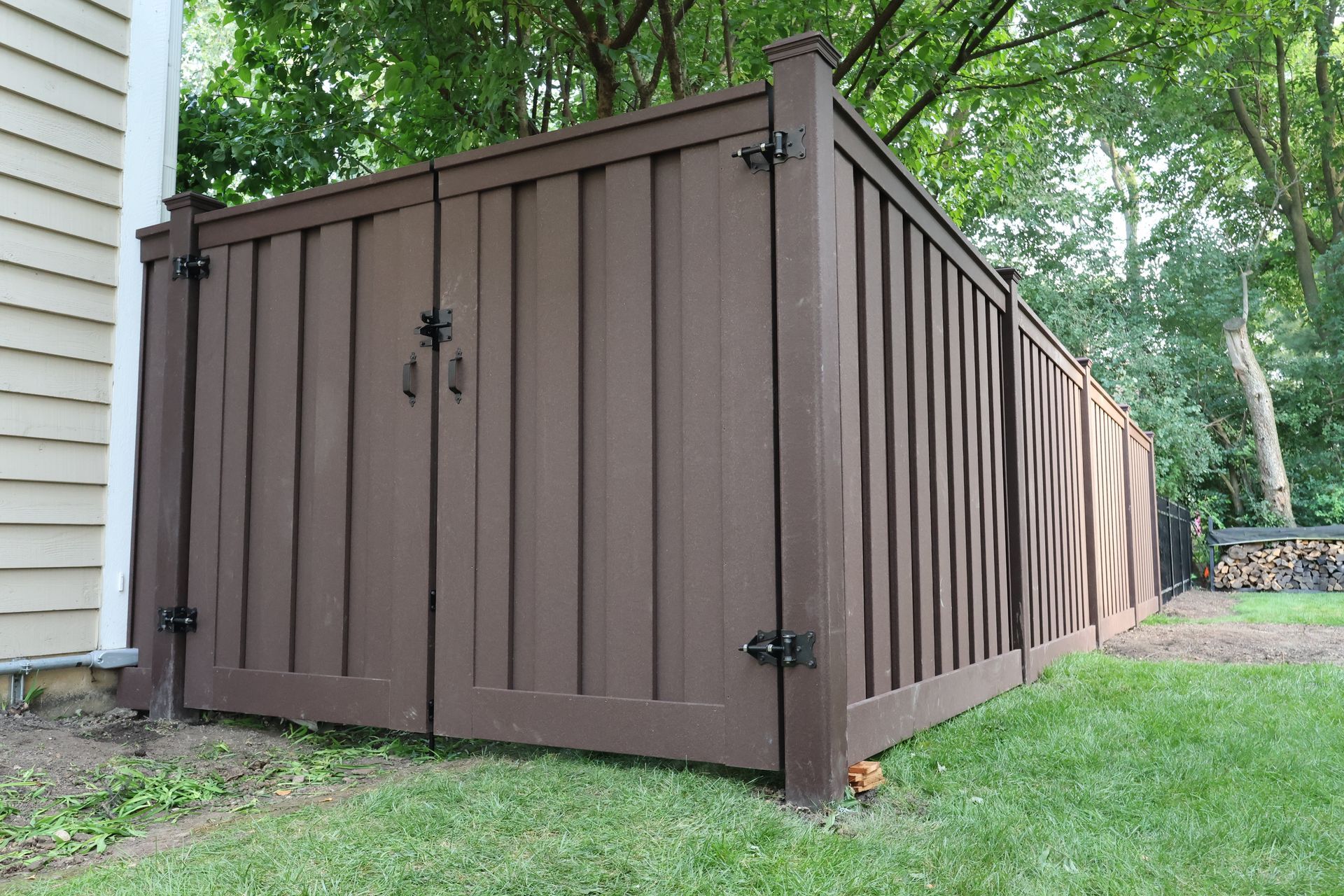 A brown composite trex fence with a gate in the backyard of a house.