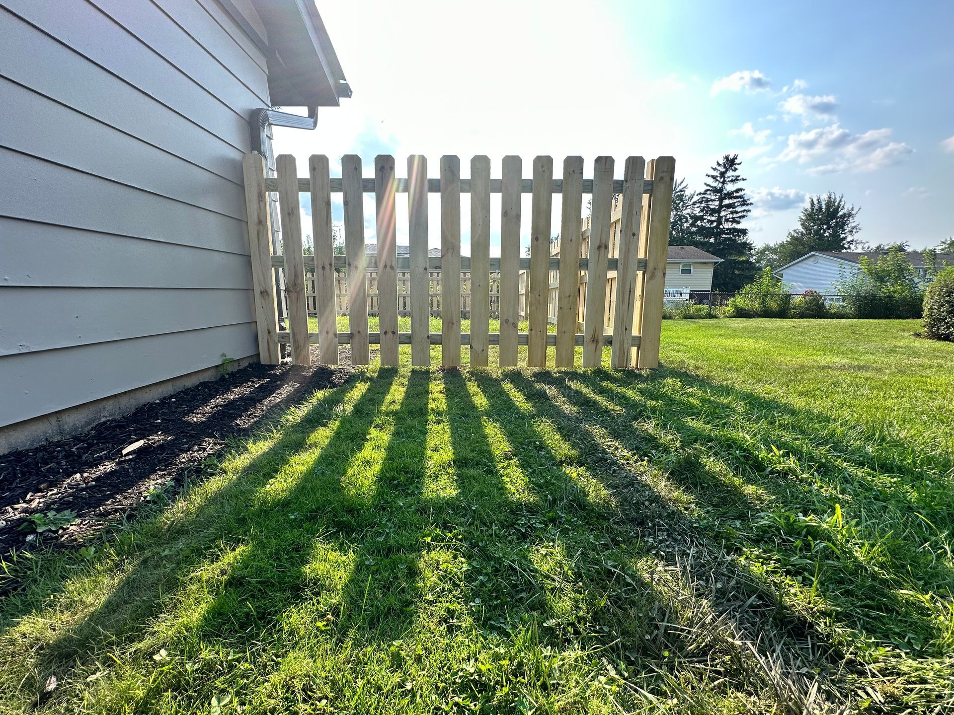 A wooden picket fence is sitting in the grass next to a house.