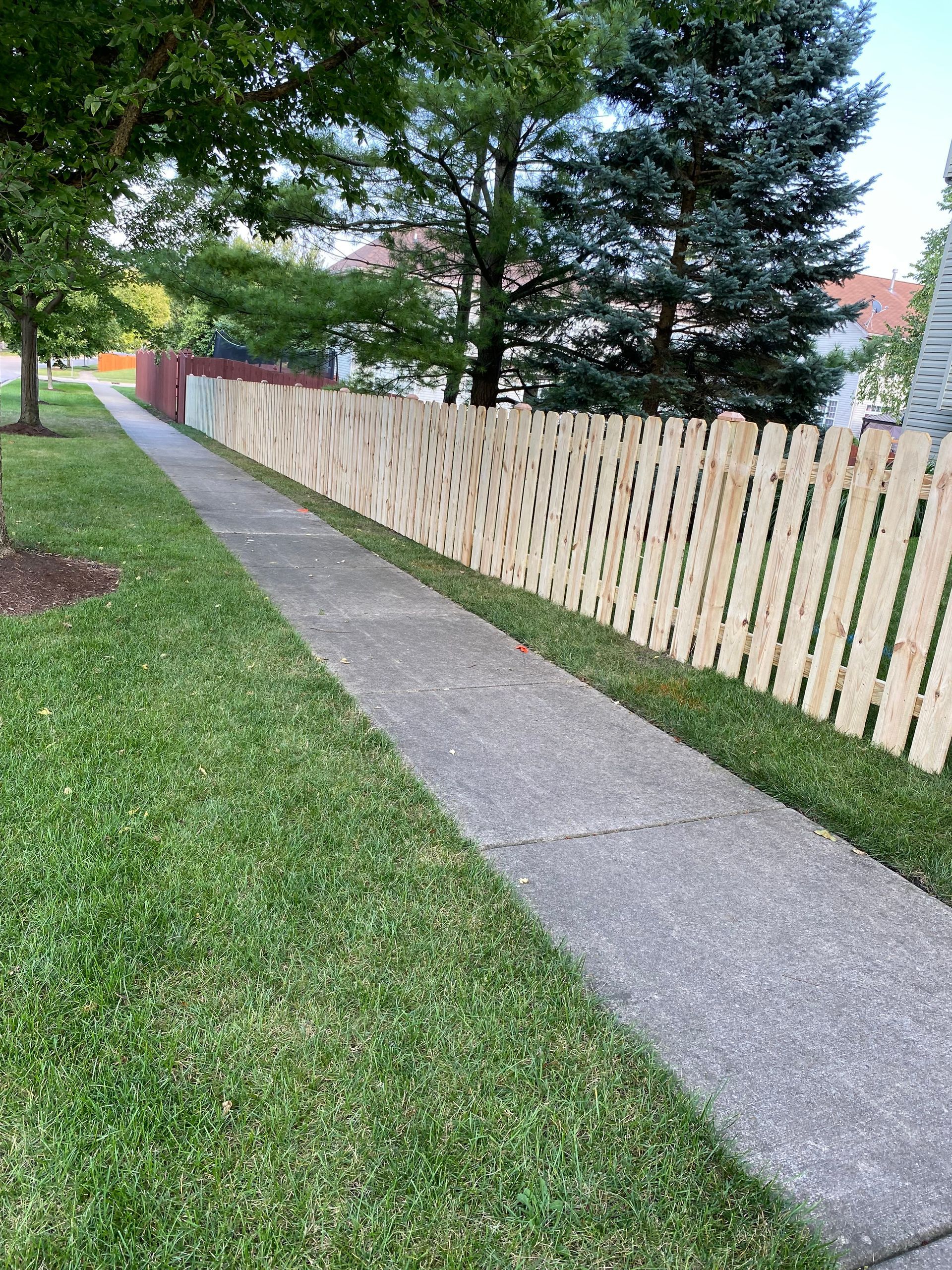 A wooden fence along a sidewalk next to a lush green lawn.